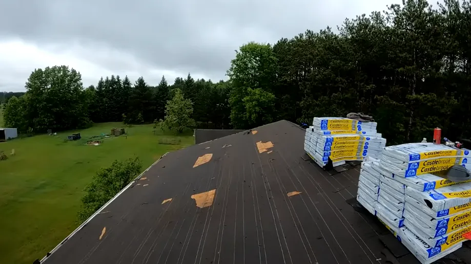 Worn asphalt shingle roof with exposed patches and new shingle bundles staged before replacement