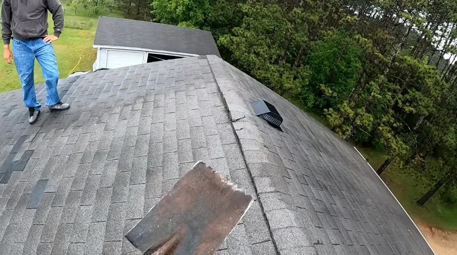 Roofer working near the ridge vent of a worn asphalt shingle roof