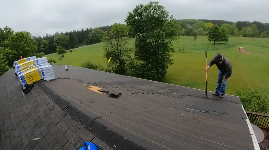 Roofer tearing off damaged shingles near the roof peak